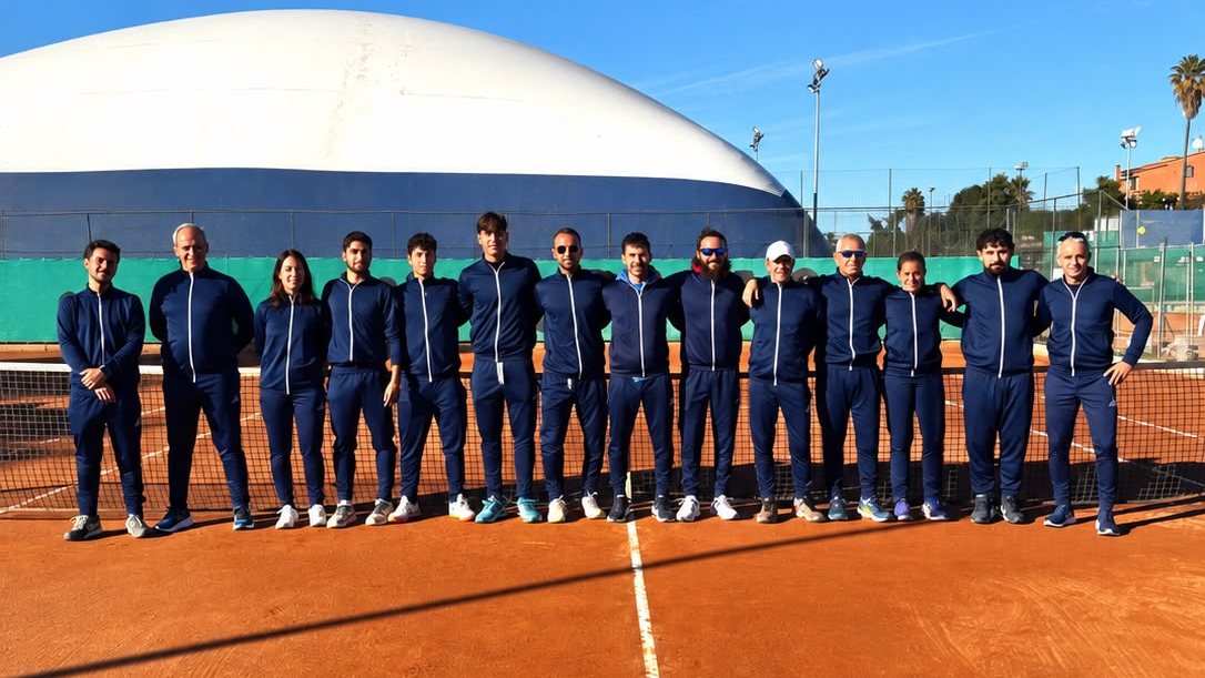 Lo staff della scuola tennis schierato sulla terra battuta, davanti al pallone del campo coperto